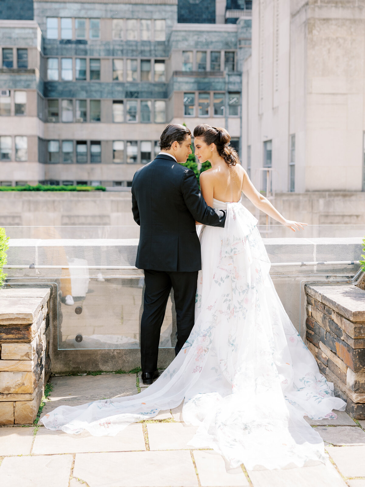 bride in Monique Lhuillier floral gown and groom in black tux stand together at rooftop wedding in New York City