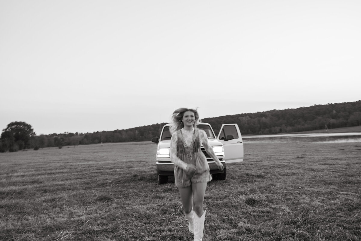 Black and white photo of a woman running through a field in—Western-inspired editorial portrait with vintage Bronco and carefree energy.