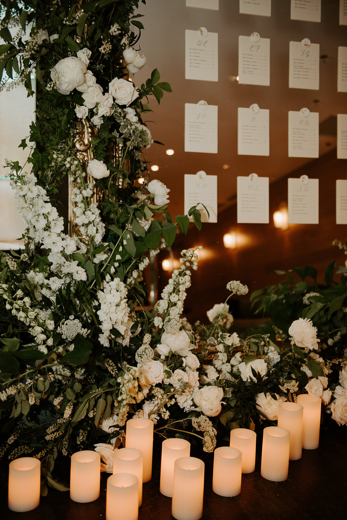 An arrangement of lush greenery and white flowers sits below a mirrored place card display at Restaurant Beatrice