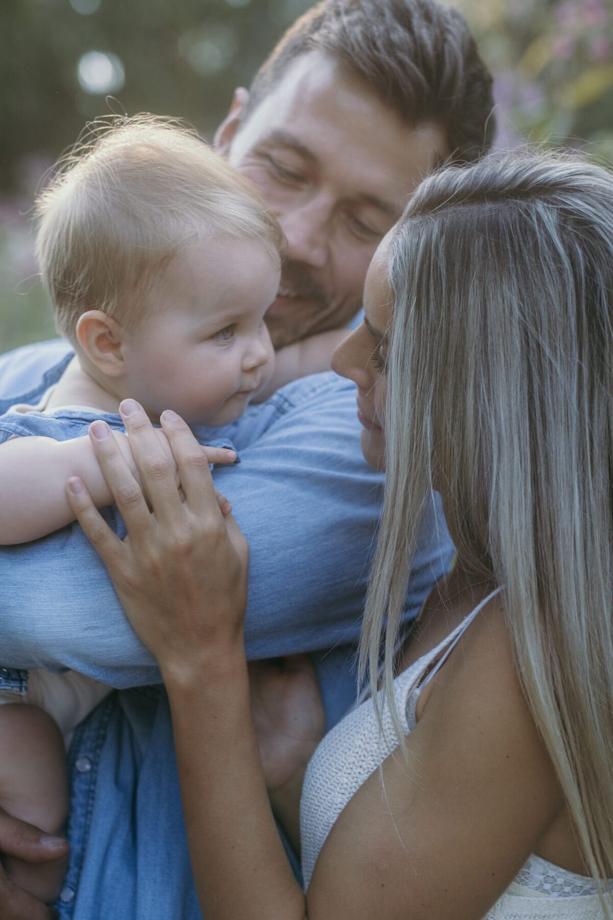 Dad holds baby, which is looking at her mom.
