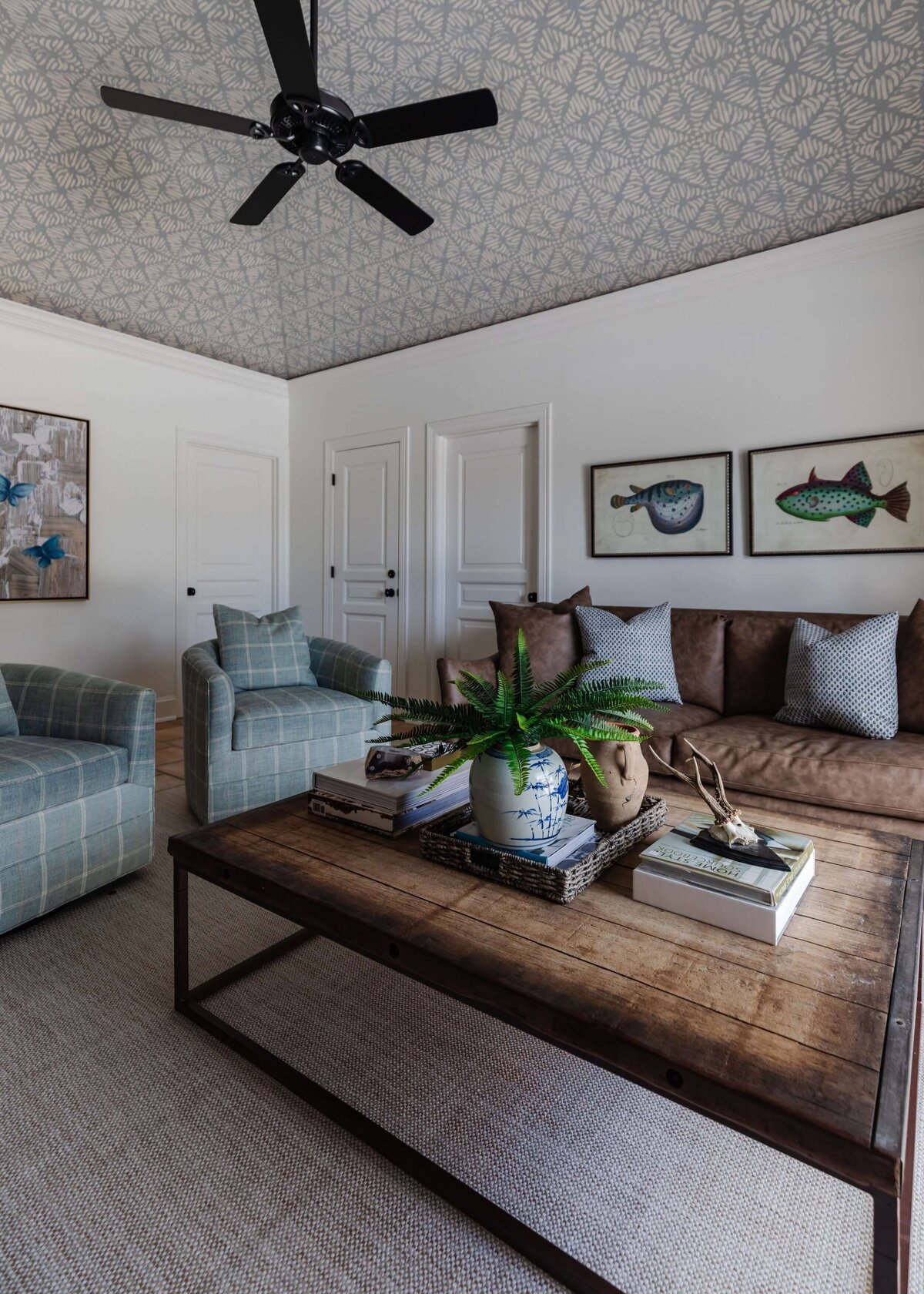 oyster creek studios home on the range wooden coffee table with blue armchairs and brown sofa in living room with fish paintings