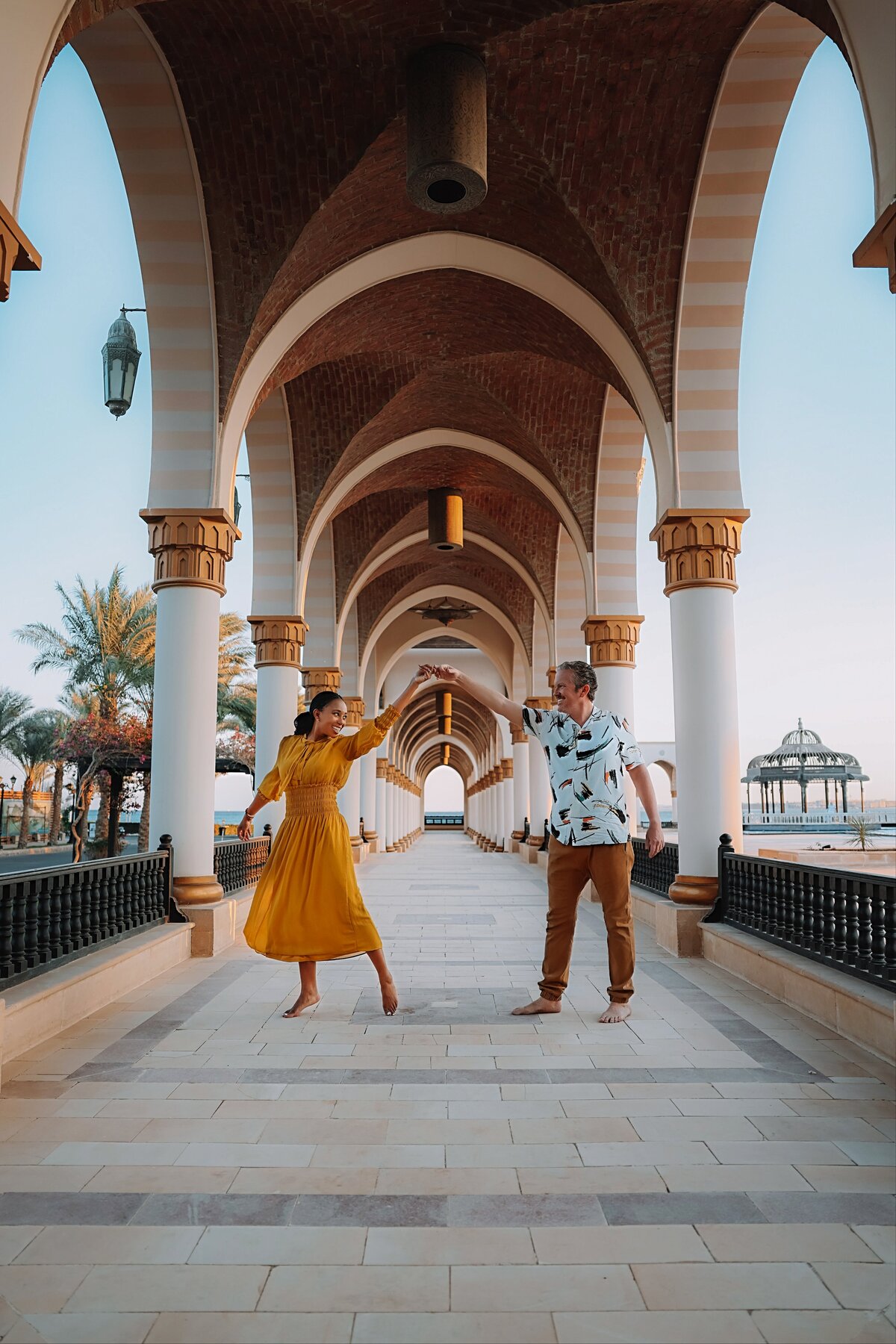 Man spins his wife in a mustard-colored dress underneath arched walkway