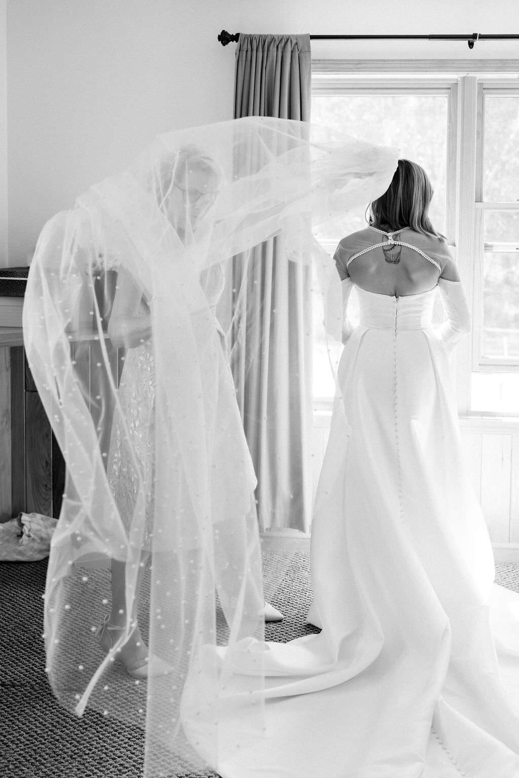 black and white photo of a woman adjusting a brides veil
