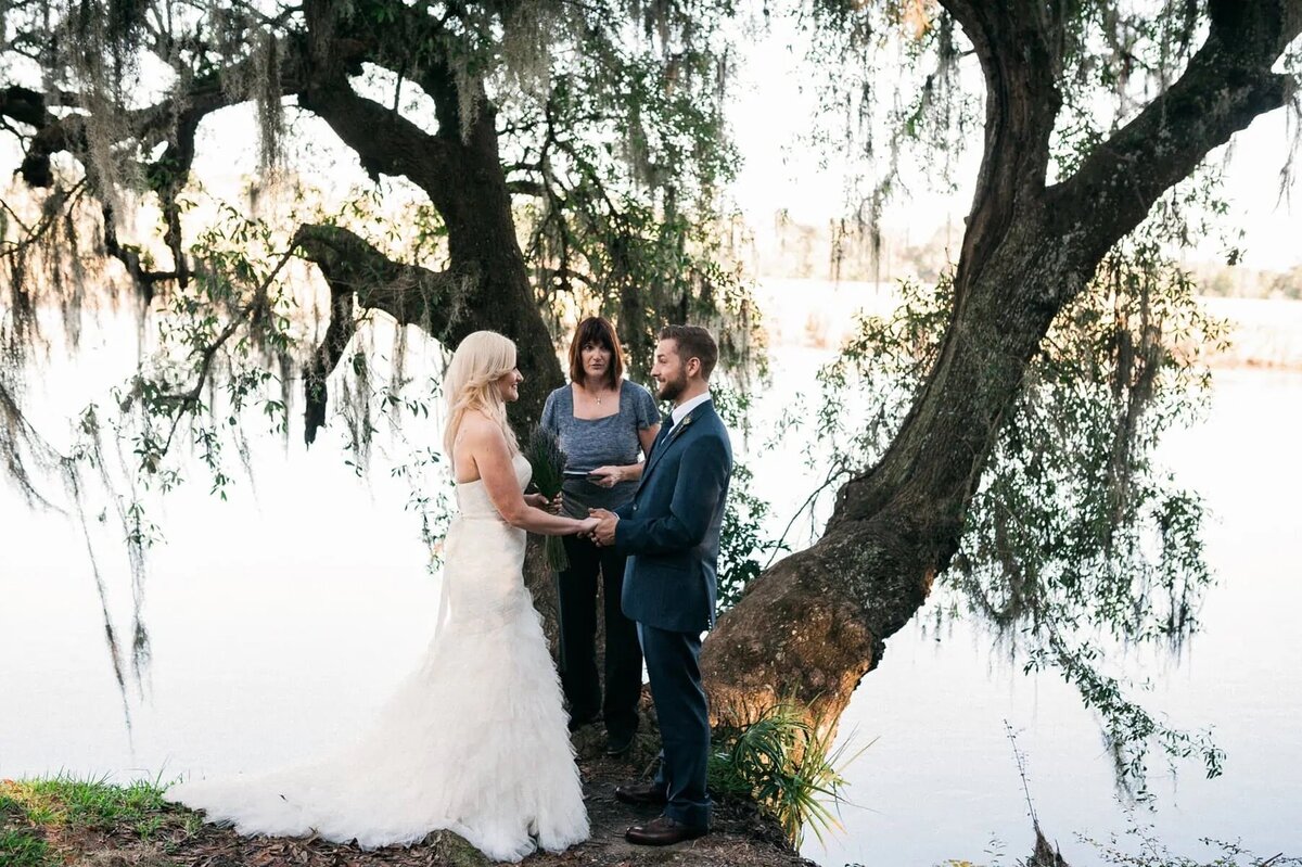 A bride and groom holding hands with an officiant behind them.