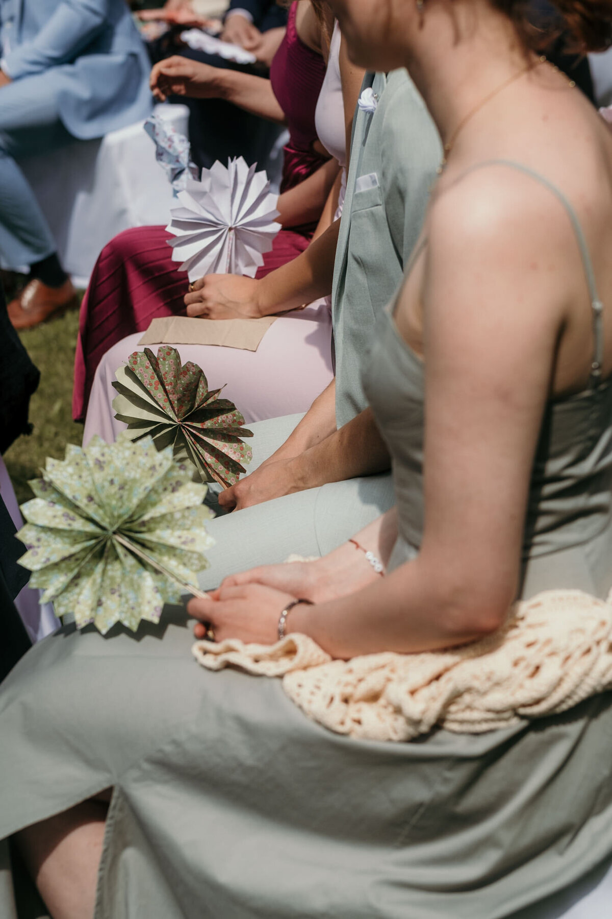 Candid moment photography of guests sitting during free wedding ceremony with fans.