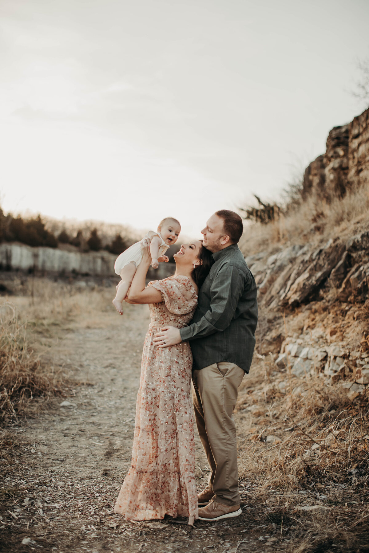 Mom and dad close to one another while mom holds baby in the air. 