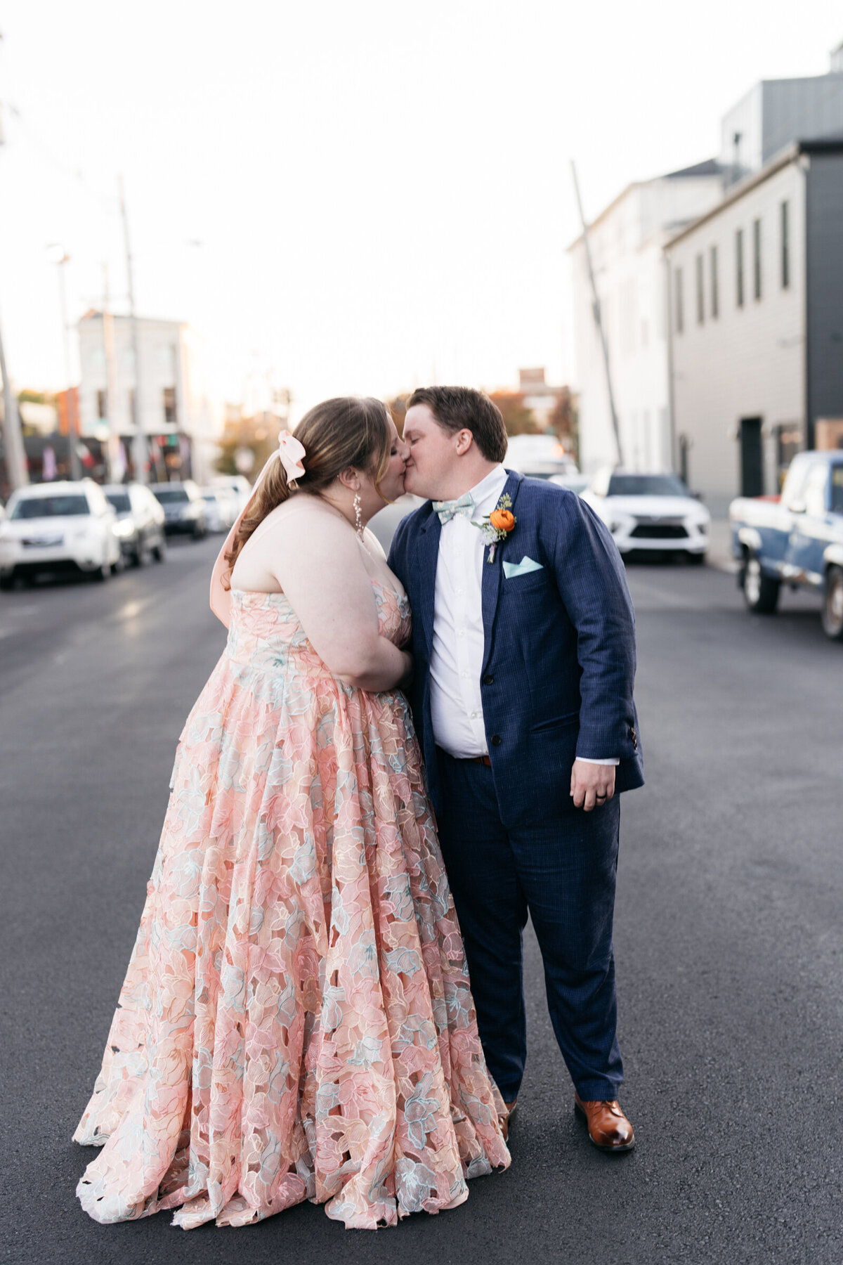 bride wearing colorful wedding dress kissing groom in blue silk suit