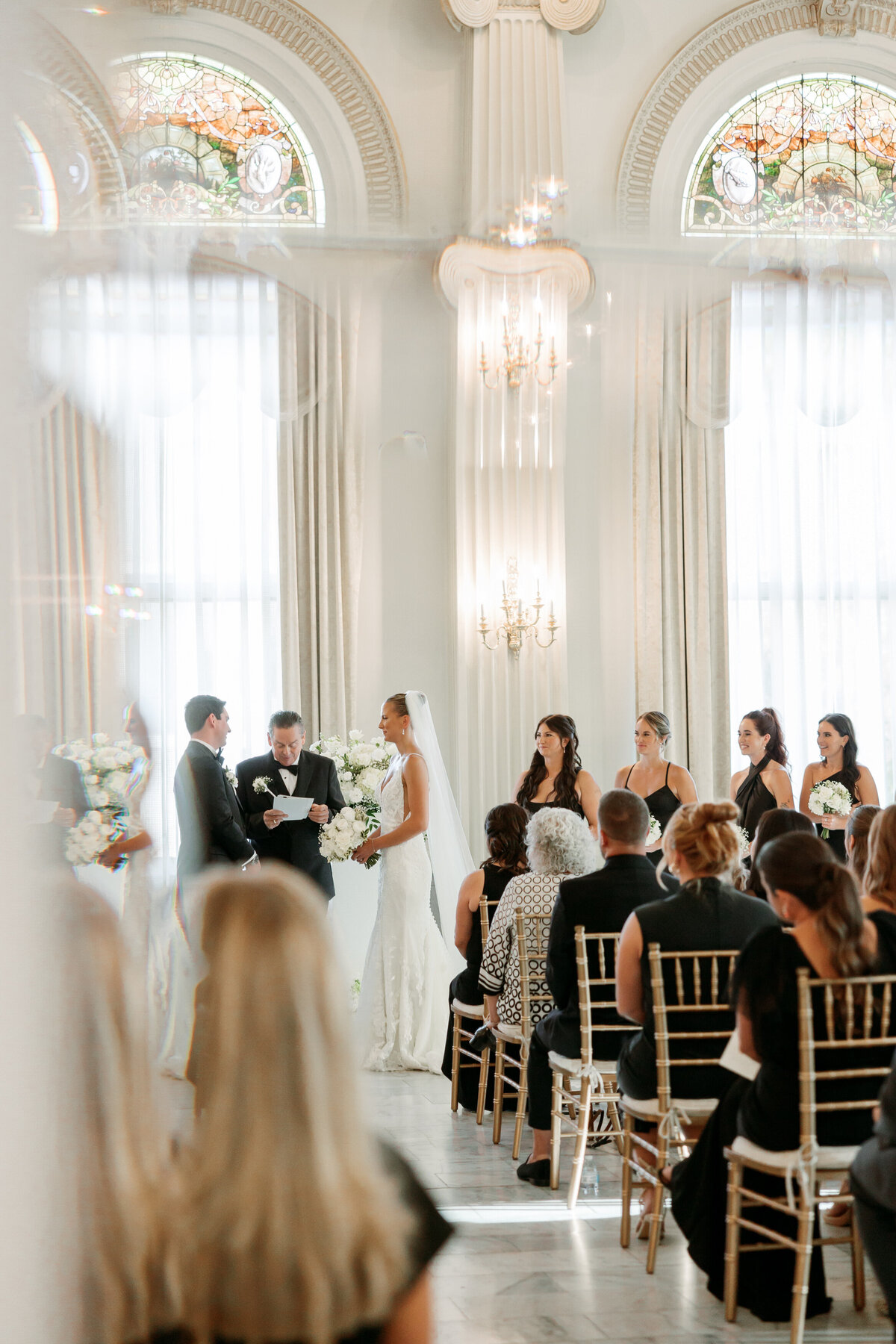Elegant ceremony scene with the couple and wedding party under tall windows and soft light, a full-room perspective by a Philadelphia wedding photographer.