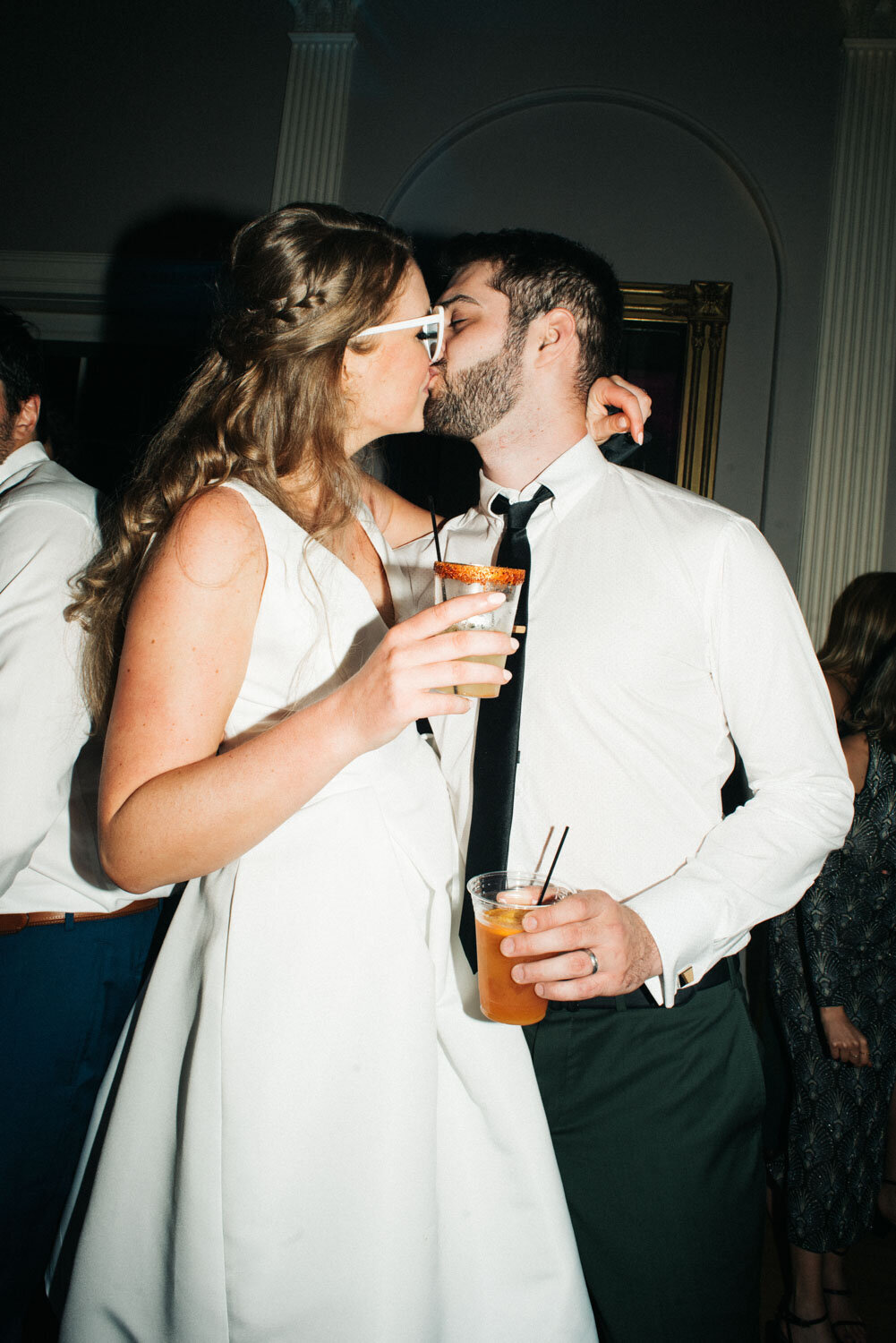 Bride and groom kissing while holding their drinks