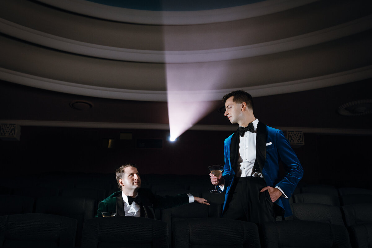 Two grooms, one sitting and the other standing looking at each other before their Regal Cinema wedding.