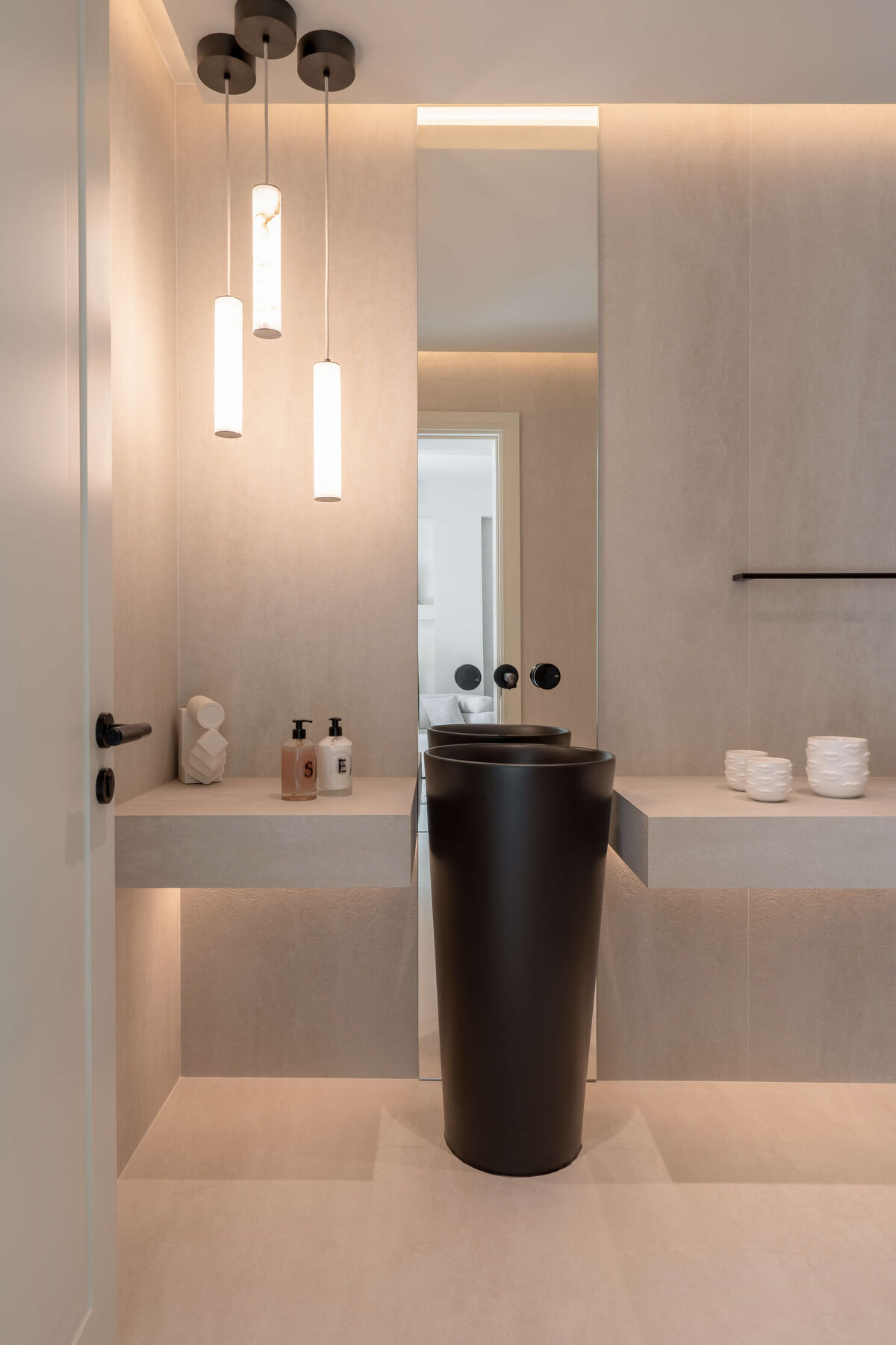 Modern bathroom featuring a light, airy aesthetic contrasted by a dramatic black pedestal sink, Three cylindrical pendant lights emit a warm glow.