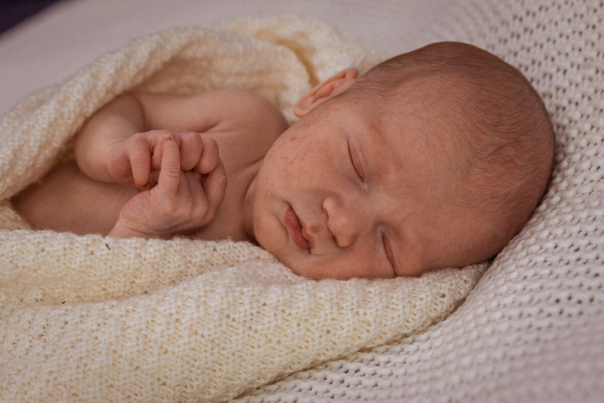 Nærbilde av baby som ligger og sover inntullet i et strikket pledd.