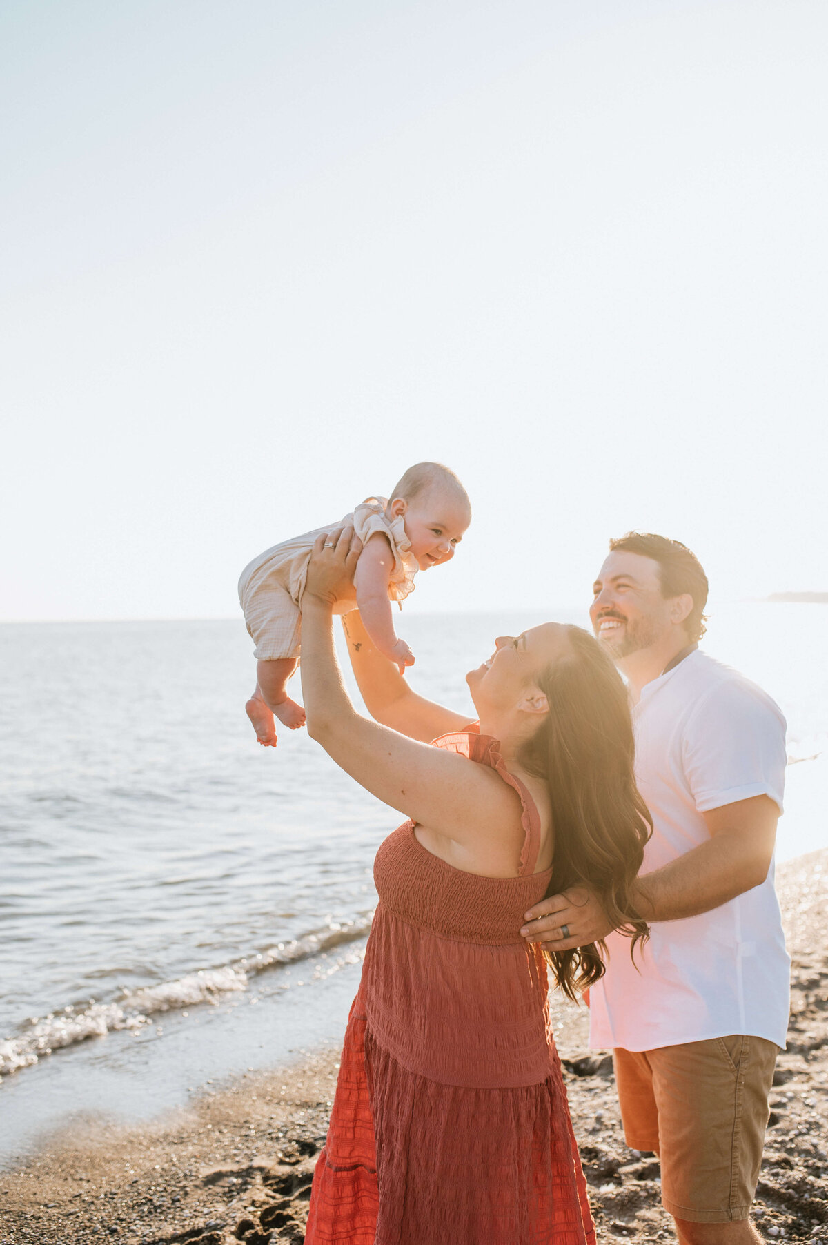 Woman-holding-baby-up-in-air-at-the-beach