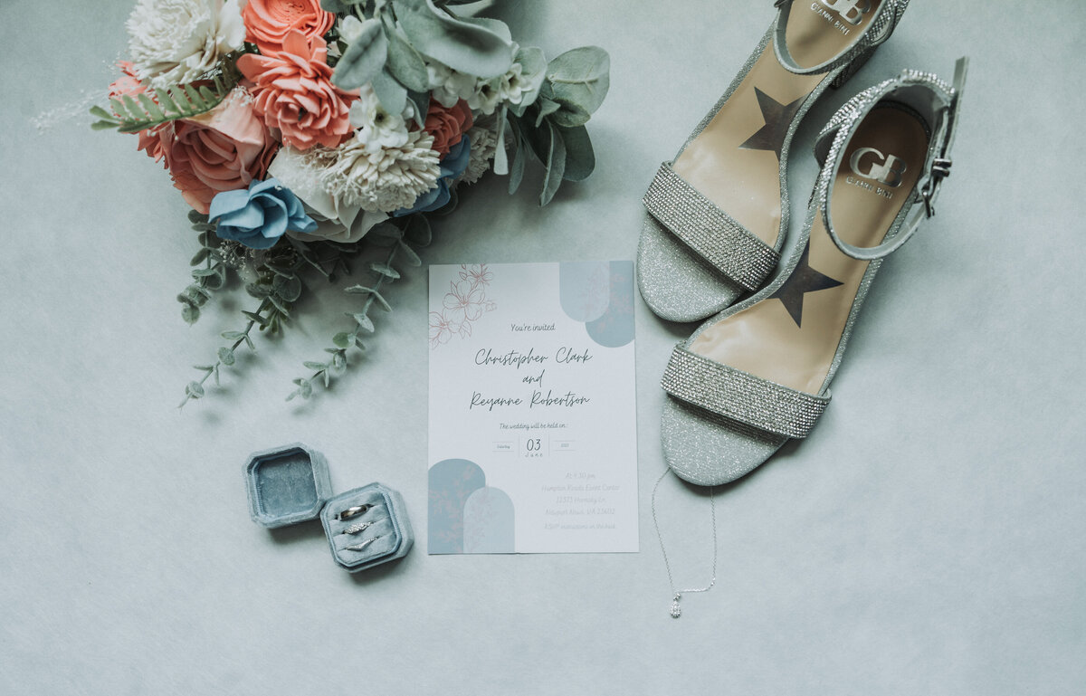 Elegant wedding day flat lay featuring sparkling bridal heels, a pastel floral bouquet, custom wedding invitations, and engagement rings, beautifully photographed at the Hampton Roads Event Center in Newport News, Virginia.