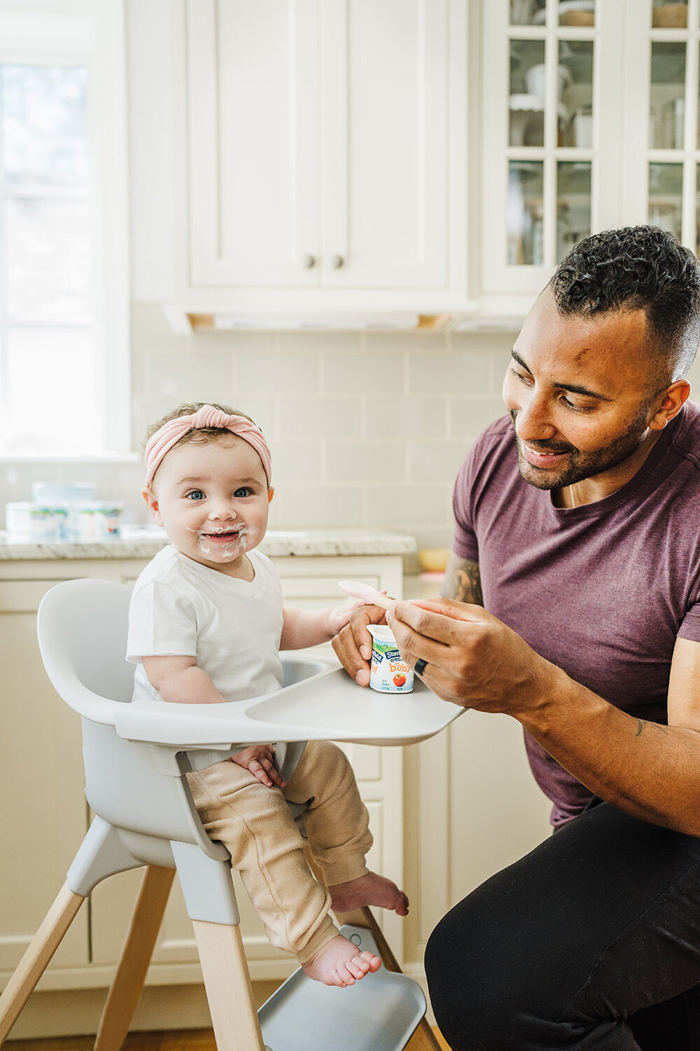 baby smiles at camera while dad feeds her yogurt