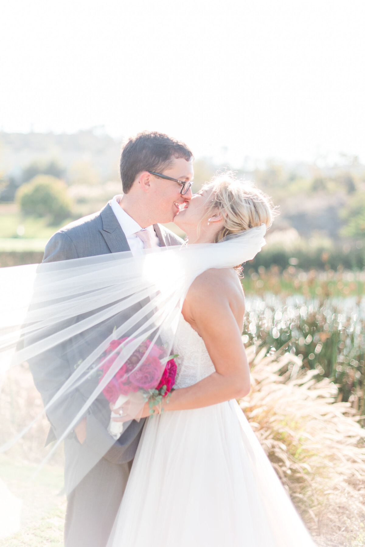 bride and groom kissing with veil blowing in the wind