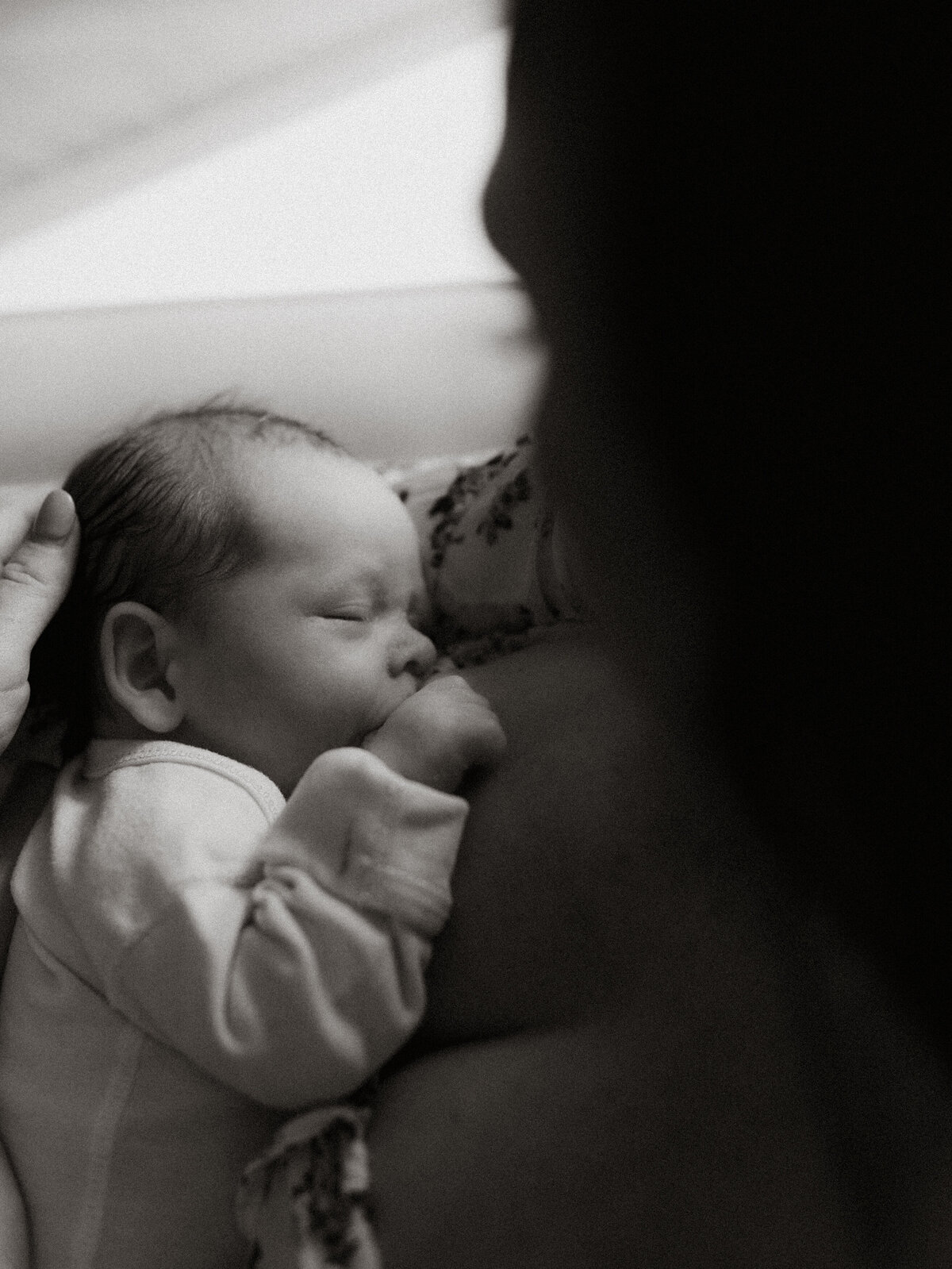 Black and white portrait of mom breastfeeding newborn while sitting in the nursery next to window light.
