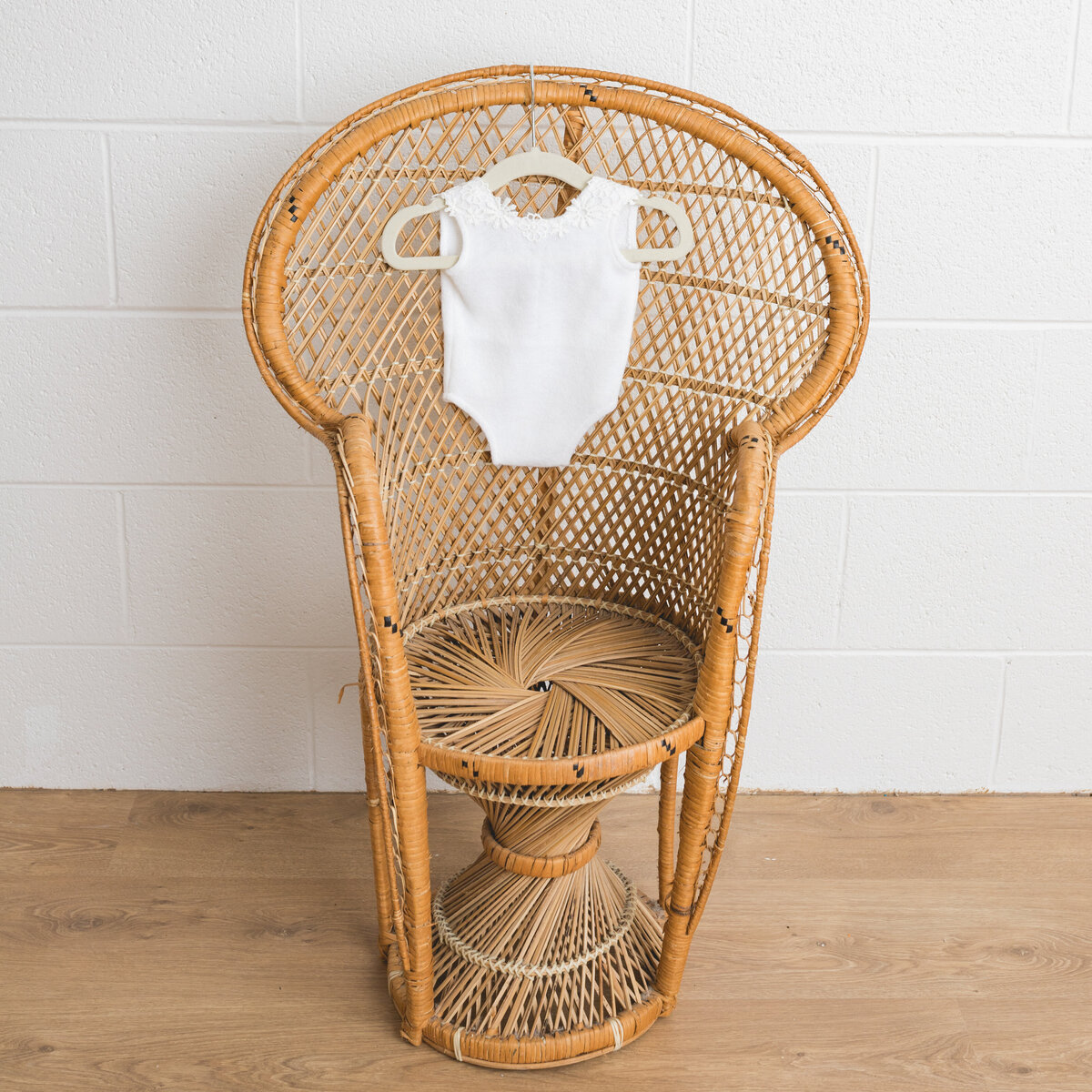 Image depicts a miniature peacock chair in a photography studio on the chair hangs a tiny newborn outfit in white knit with embroidered flowers.  This image is a sample of Lauren Vanier Photography's newborn client wardrobe. Image taken in Hobart Tasmania.
