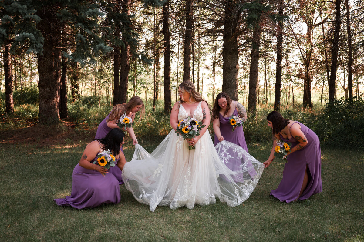 Bride standing in a field while 4 bridesmaids adjust her dress and get her ready for wedding 