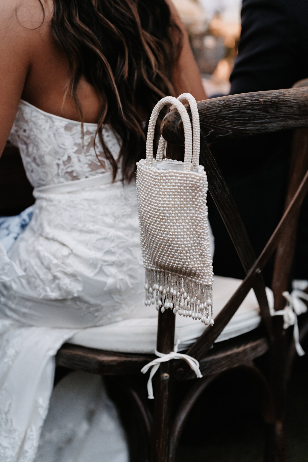 Brides purse hanging on the back of a dark wood chair, she is sitting in a strapless dress
