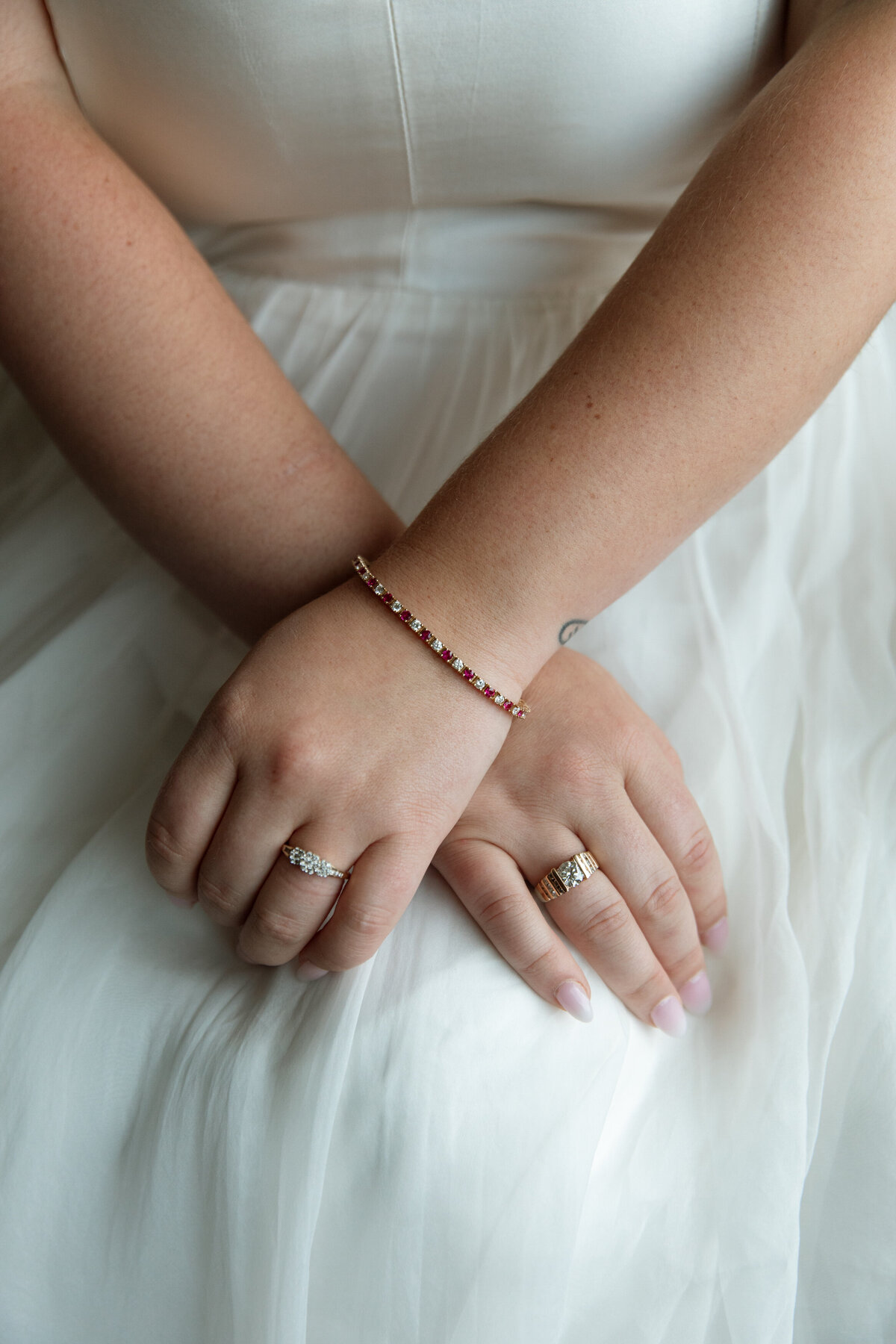 Bride sits with her hands crossed over her wedding dress for a close up photo of her rings
