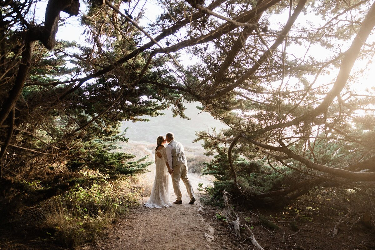 The bride and groom kiss under sycamore trees in Big sur for their elopement