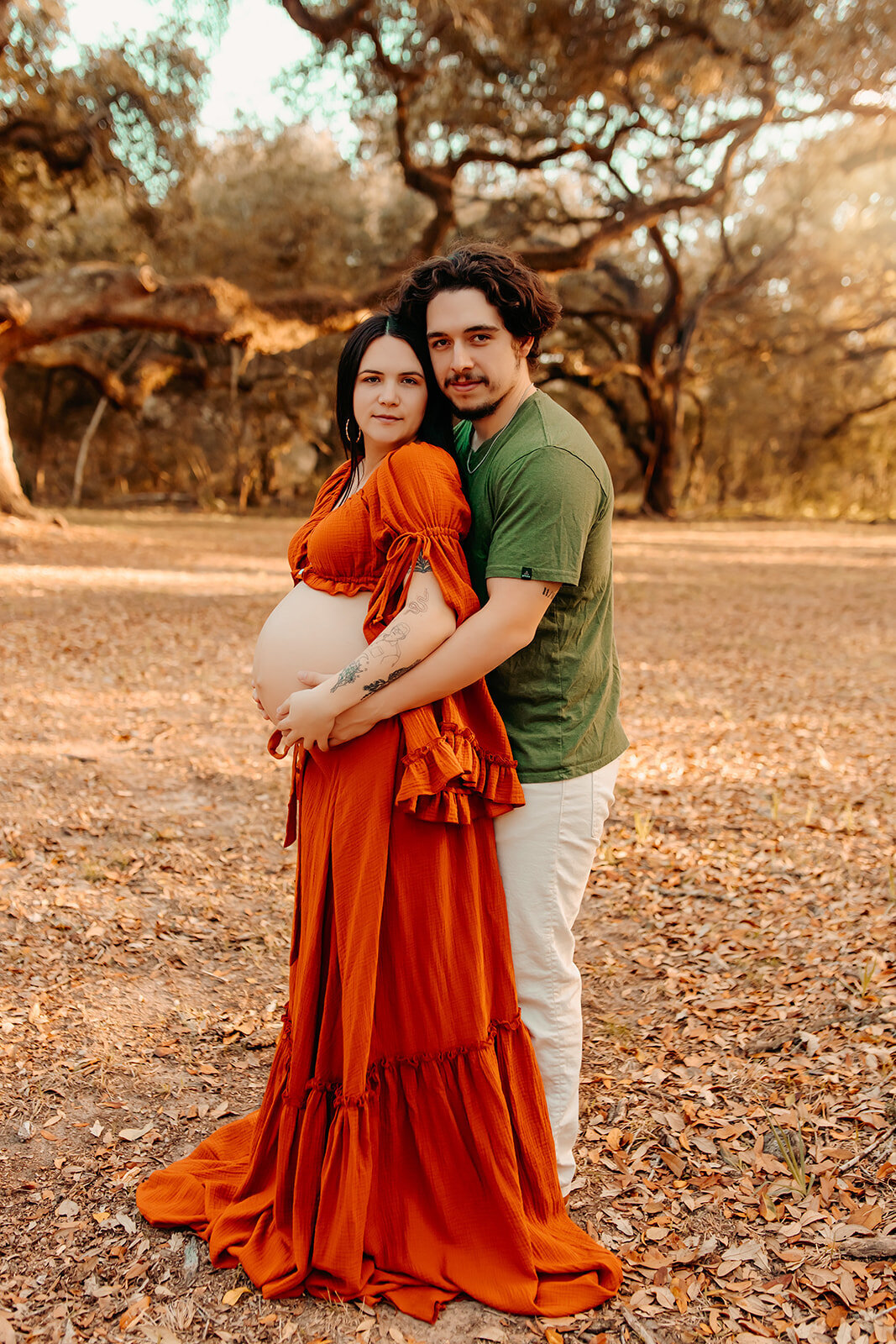 Maternity photography in Cleveland TX – expecting couple embracing under oak trees in burnt orange gown