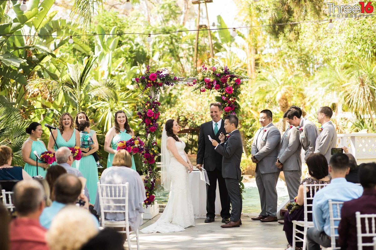 Bride and Bridal Party laugh as Groom reads his vows to her