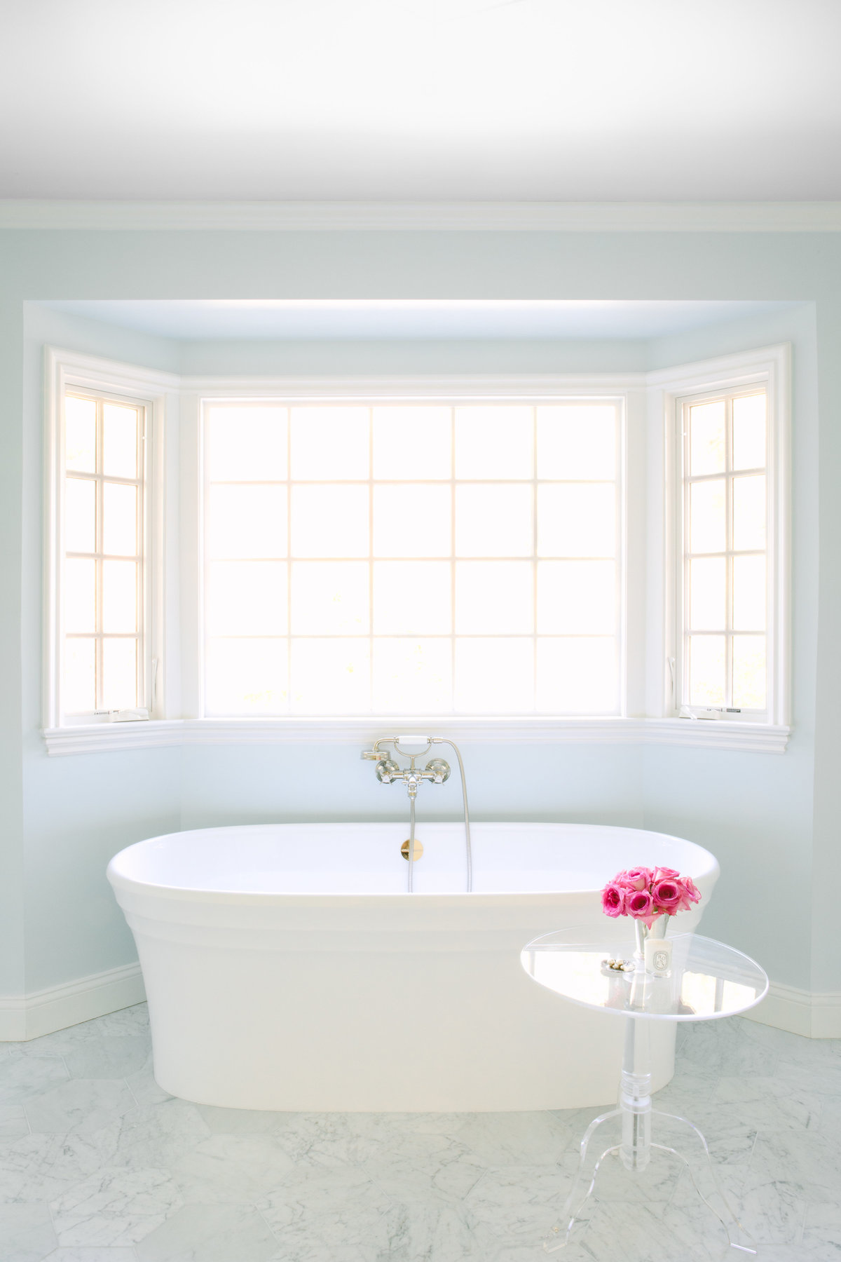 Bathroom with light blue walls, free standing Victoria and Albert tub, Lucite table, and Carrara marble hexagon floor