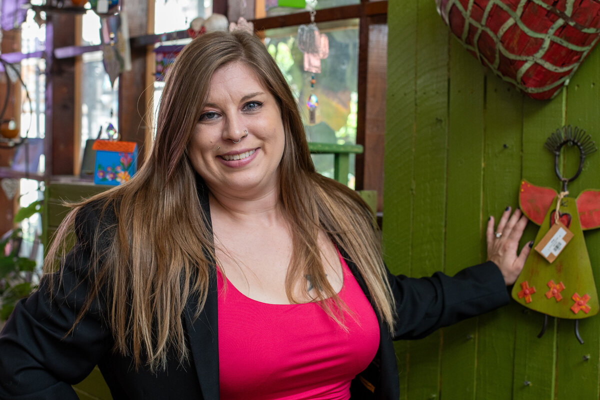 Smiling woman wearing a pink top and black blazer posing indoors beside colorful handmade décor, photographed by Vyrl Photo, showcasing Tucson brand photography.