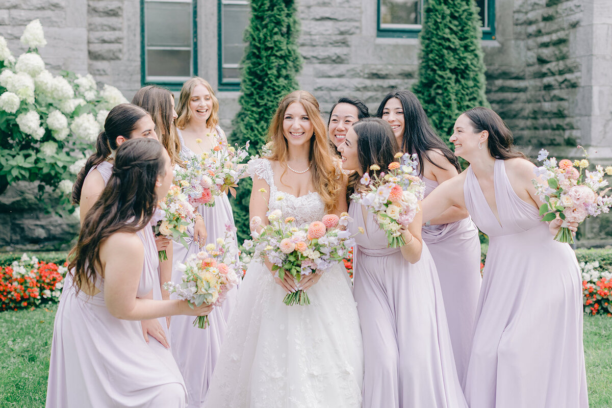 A group of bridesmaids in purple dresses hold bright pastel bouquets at the Forest and Stream Club.