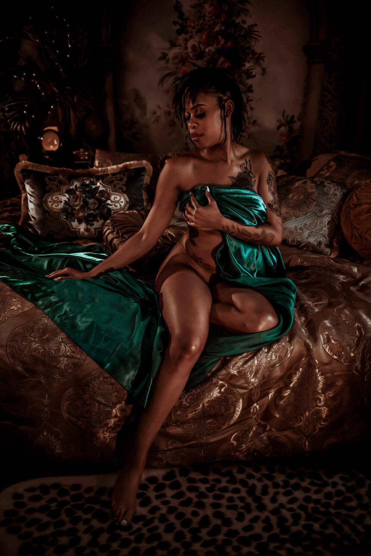 Woman wrapped in a teal satin sheet sitting on a bed in a baroque boudoir studio near DFW