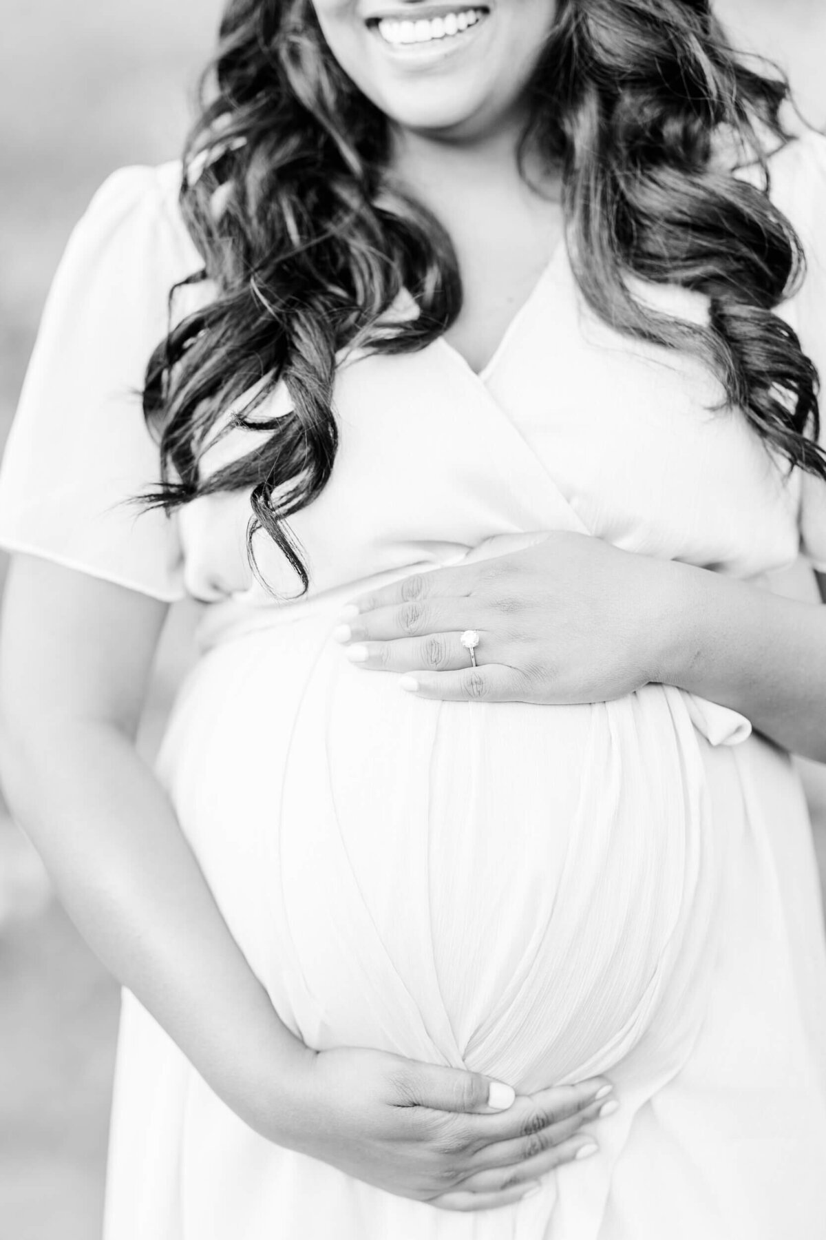 Close-up black and white image of a pregnant baby bump, with one of mom's hands above the bump and one below