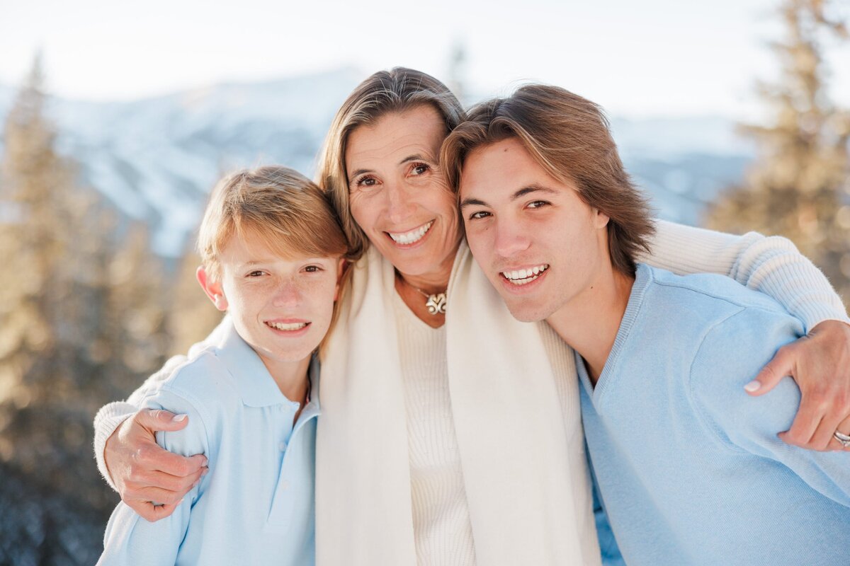 A happy mom snuggles her teen sons on a mountain overlook