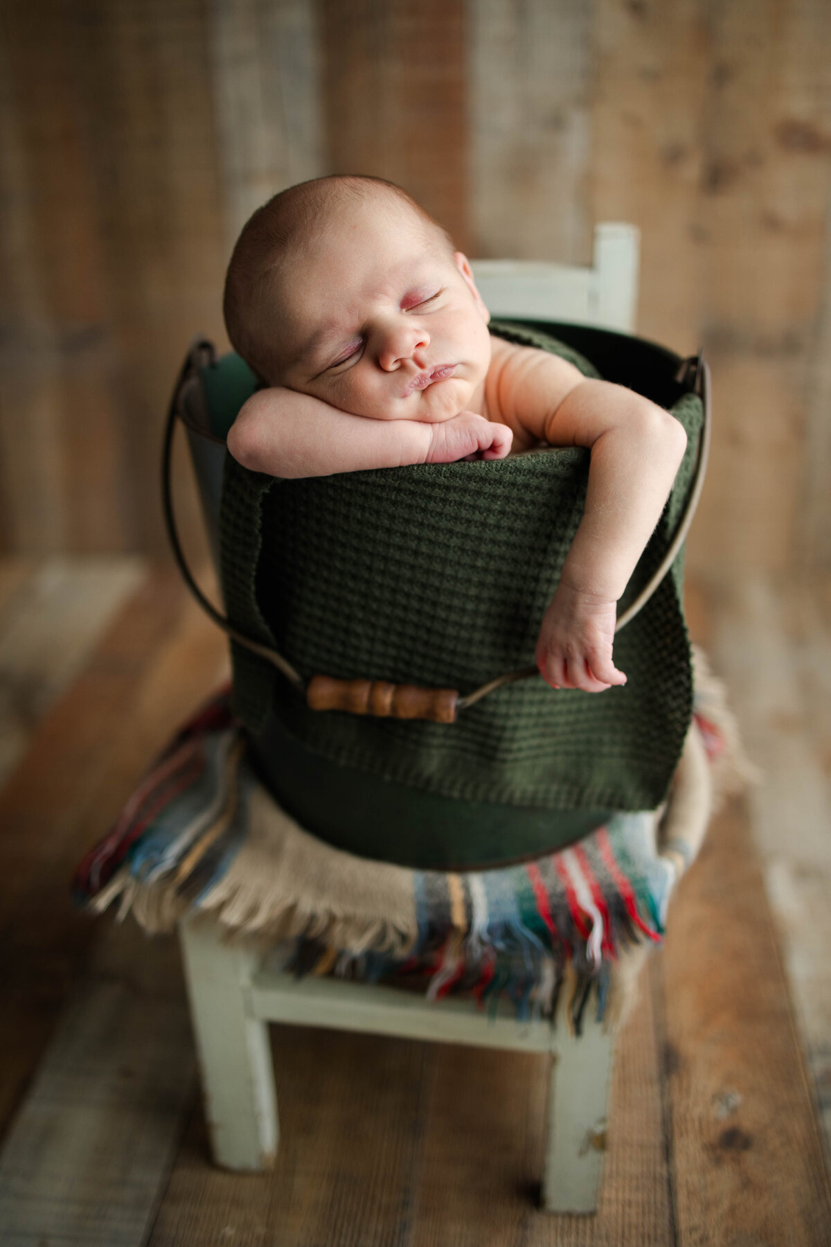 Sleeping baby boy in a green bucket with his arm hanging over