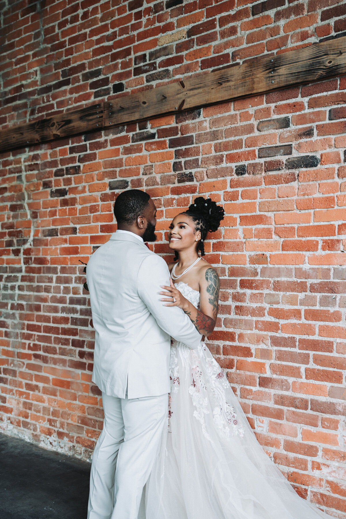 A newlywed couple embraces lovingly against an exposed brick wall at the industrial-chic Neon House in Norfolk, Virginia, sharing a tender gaze on their wedding day, captured by Quinn Photography LLC.