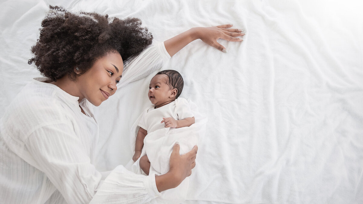 A Black mother is laying down smiling at her newborn baby.