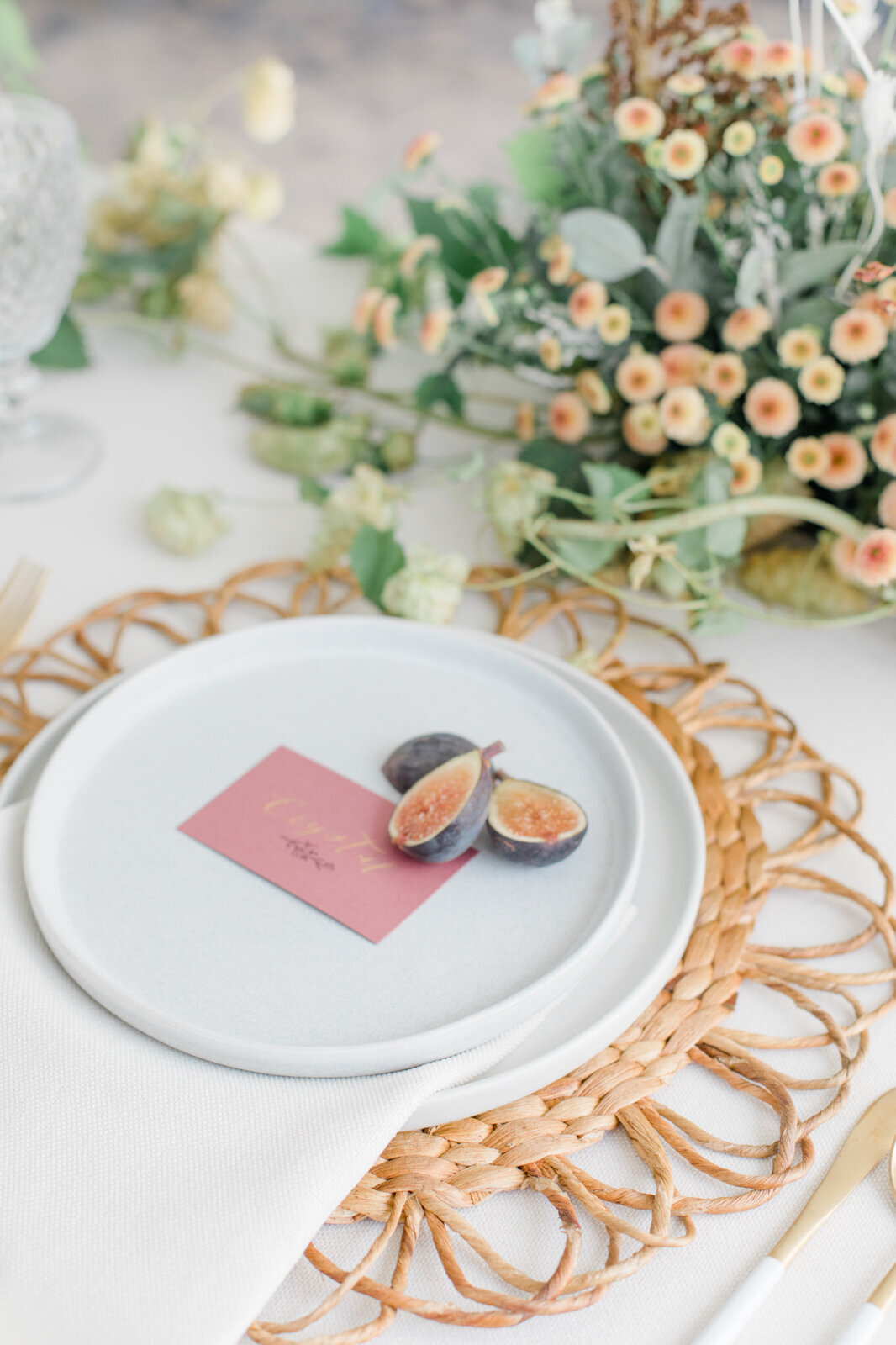 Stunning wedding reception place setting, daisy rattan charger, elegant white dinner plate, name tag, and purple pears, captured by Ana Douglas Photography, timeless and authentic wedding photographer in Vancouver, BC. Featured on the Bronte Bride Vendor Guide.