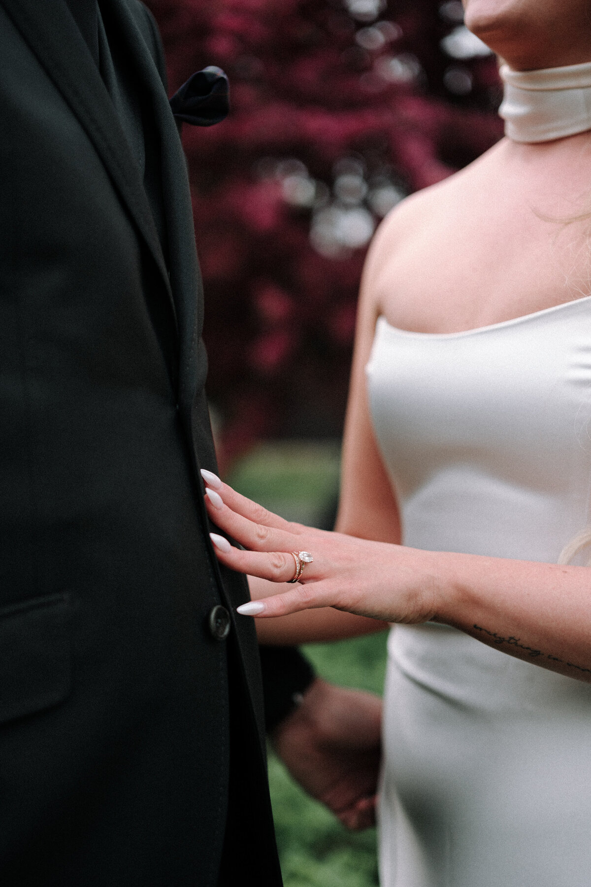 bride runs her hand down groom's suit showing ring