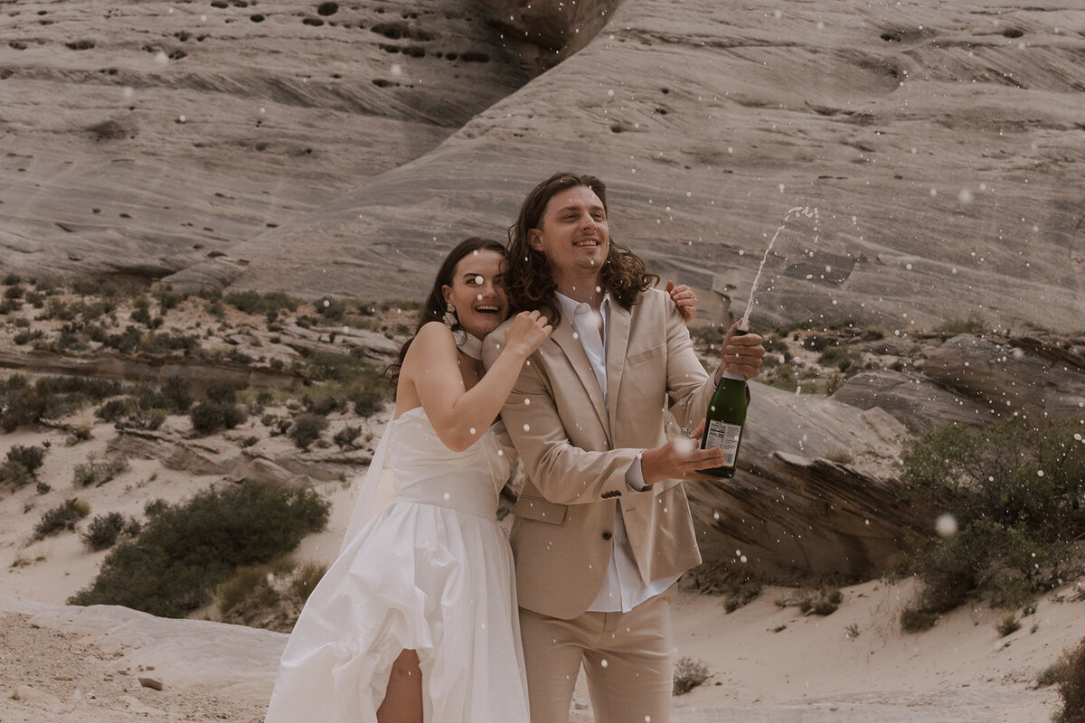 Bride and groom popping champagne in desert canyon