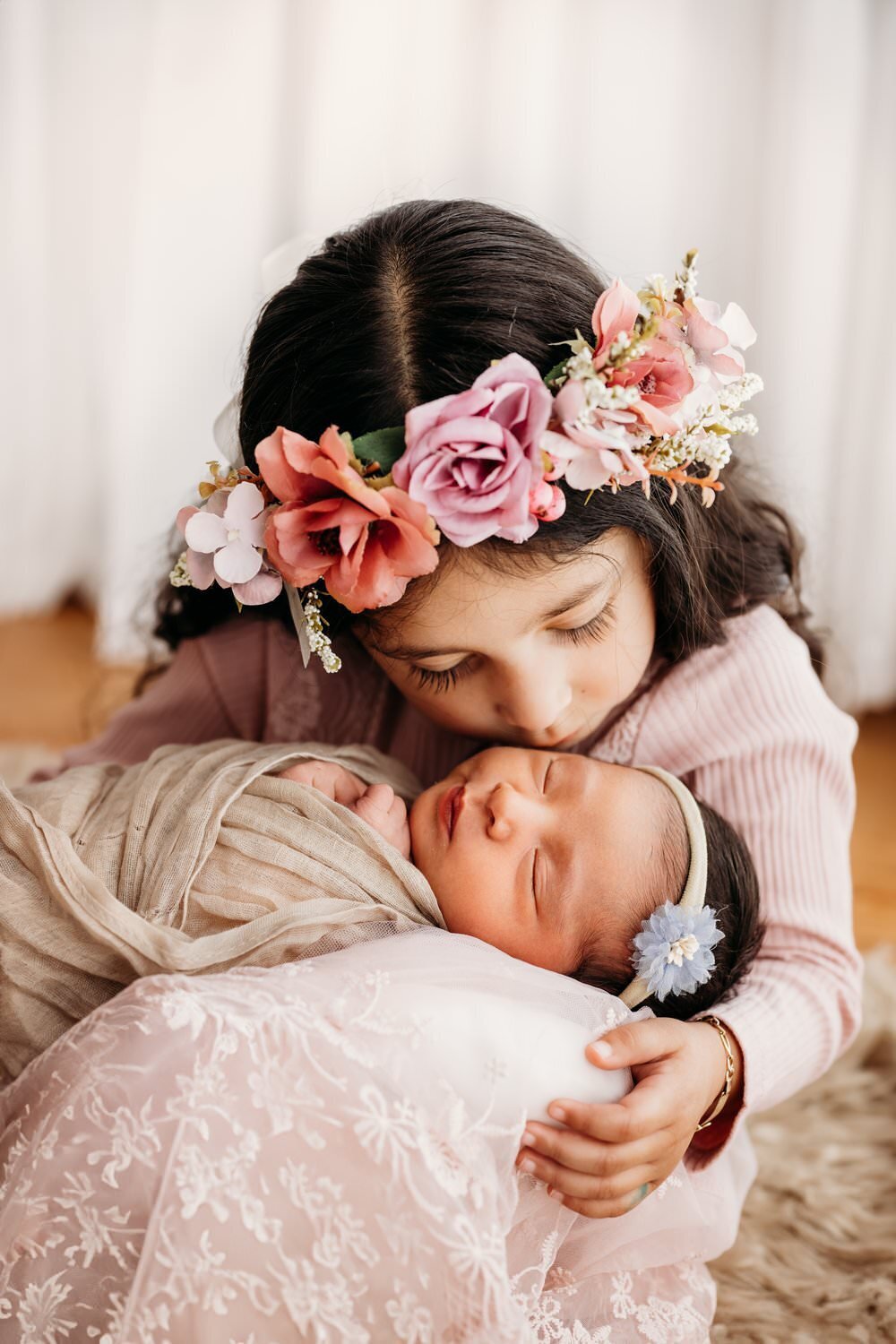 baby sister in big sisters arms. the older sister is kissing the baby