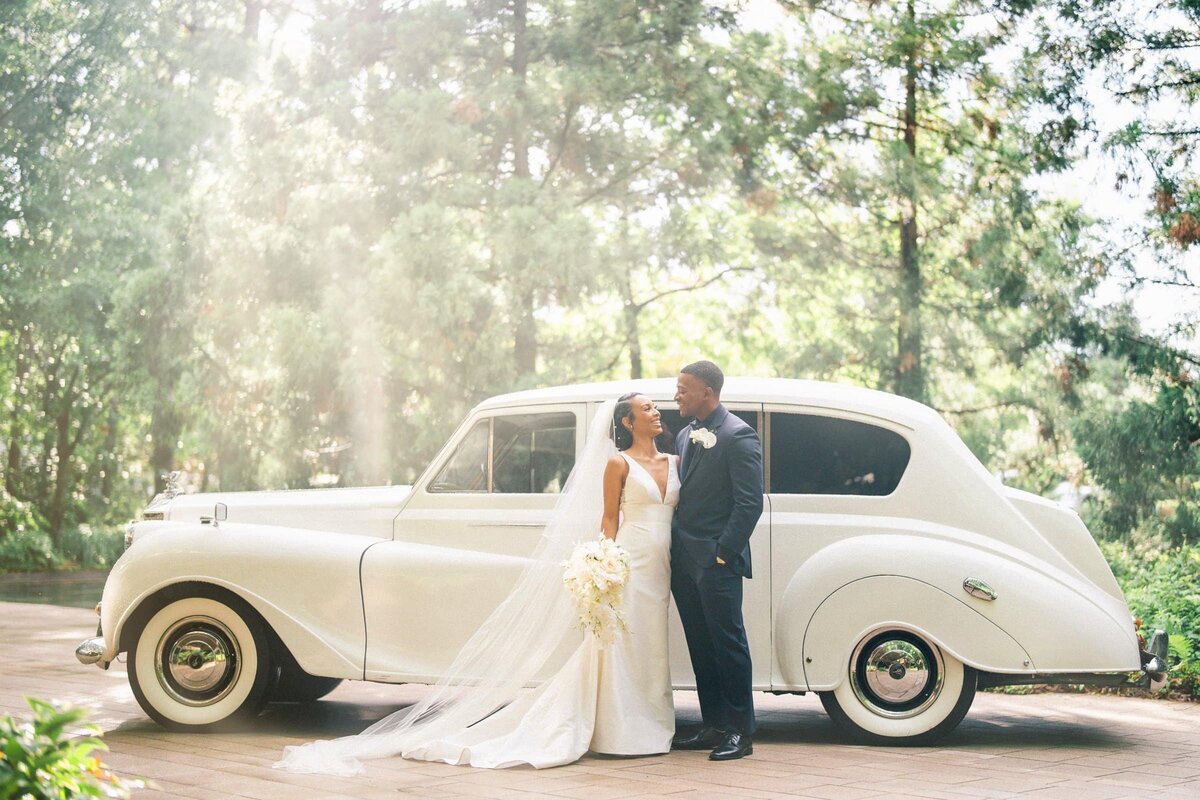 Bride and groom standing in front of a white vintage car.