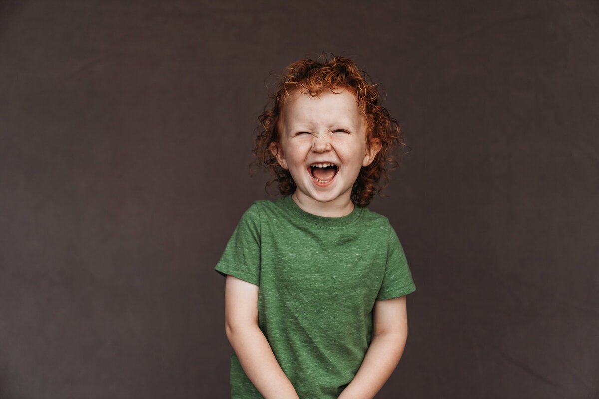 A little redheaded boy wearing a green shirt laughs uproariously while his fine art school photo is being taken in San Diego. 