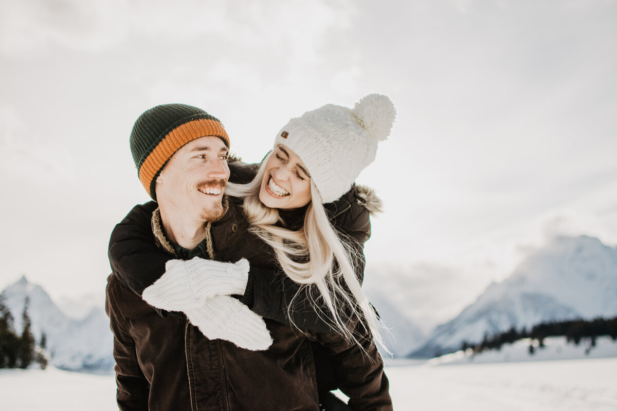 woman piggybacking on her fiances back during the JAckson HOle winter engagement session while laughing