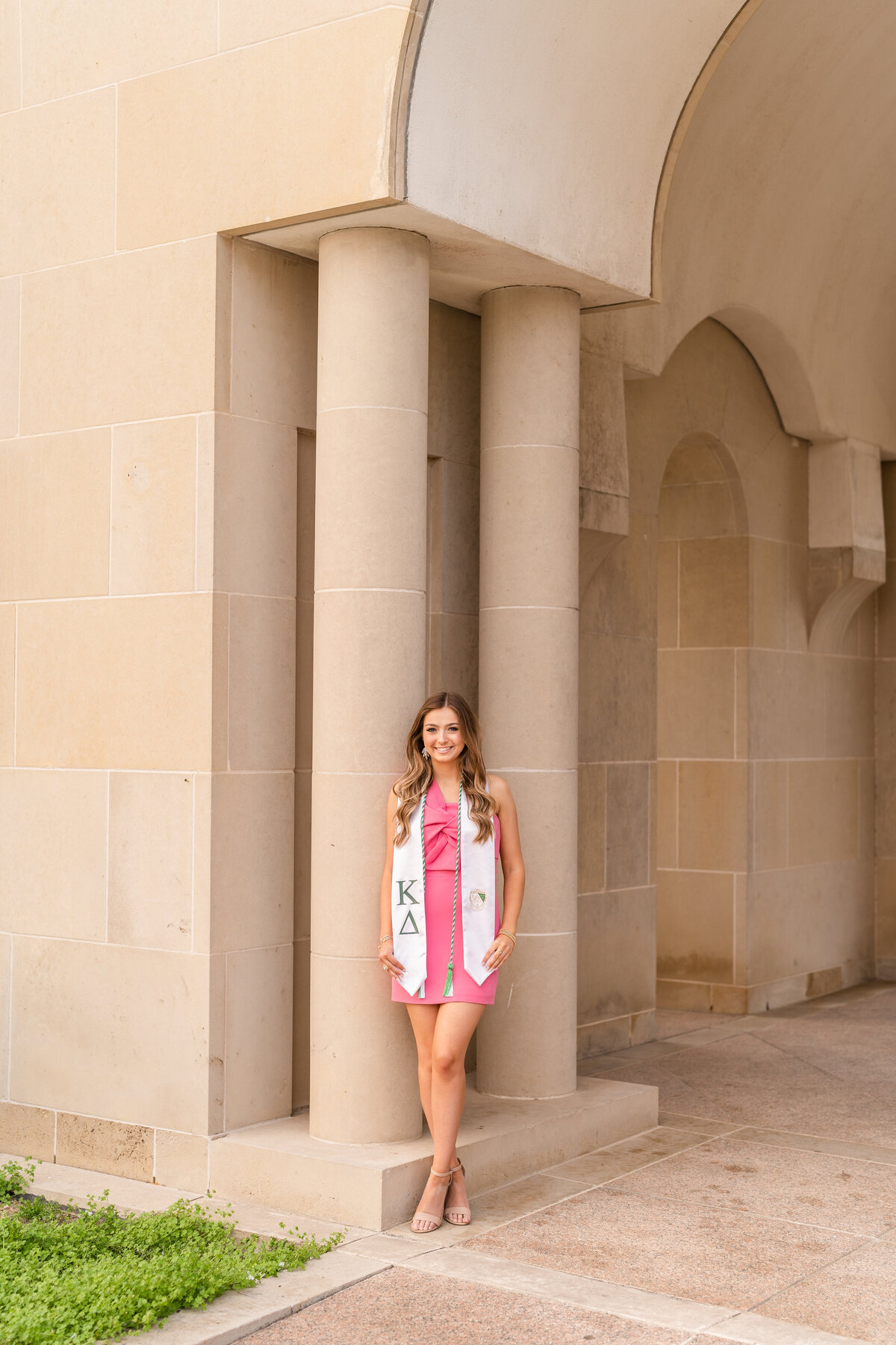 Texas A&M senior girl leaning against wall while holding Kappa Delta stole and cords at Bell Tower