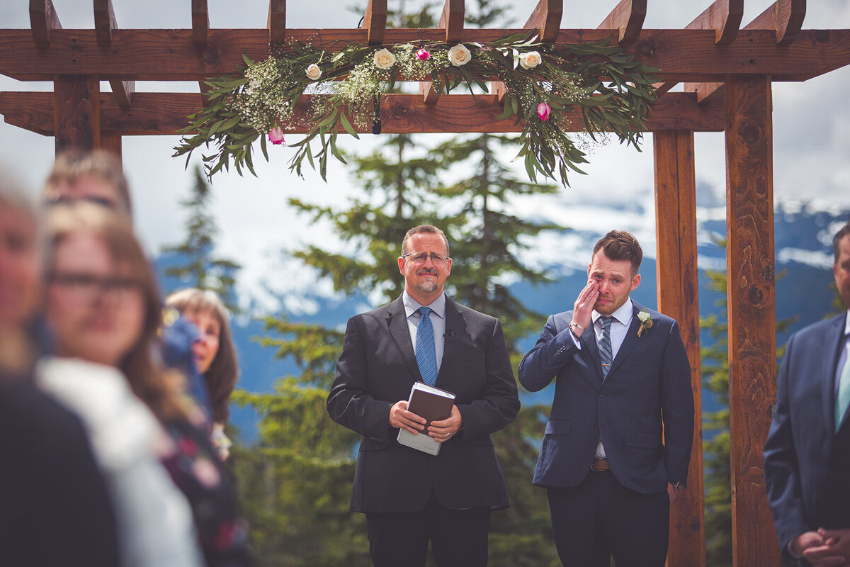 A photo of the groom, officiant, and wedding guests watching the bride walk down the aisle.