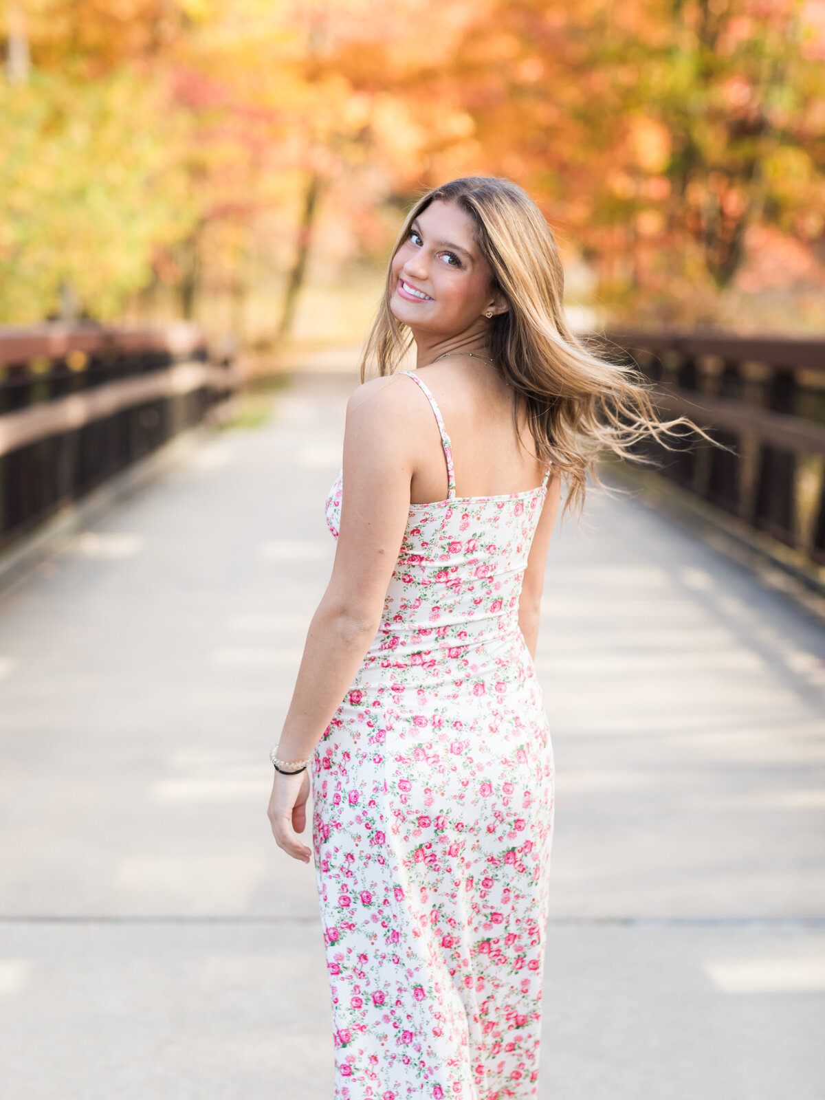 senior girl in floral dress posing on bridge for senior portraits at Westcreek Reservation in Parma, Ohio