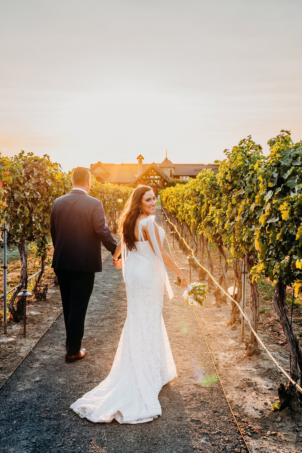 a bride and room walking through a vineyard, bride looking back at camera