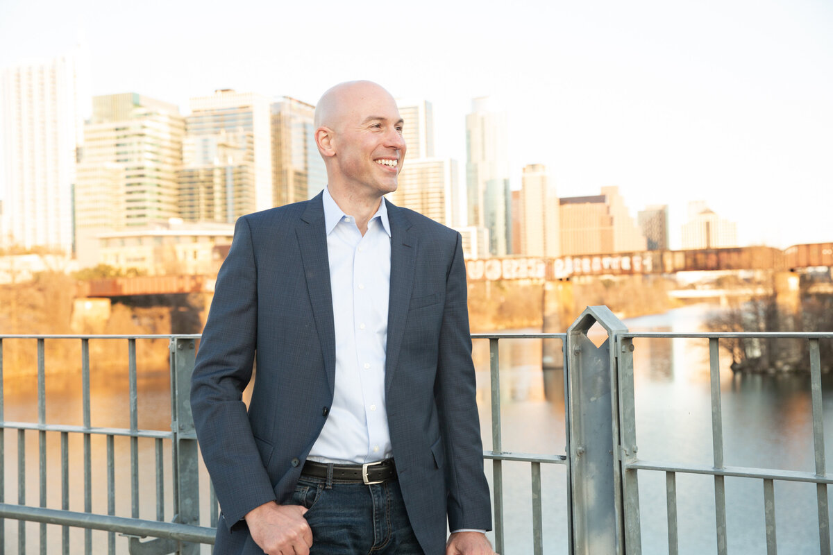A professional Austin wedding photographer captures a bald man in a suit standing on a bridge, with the stunning cityscape as the perfect backdrop.