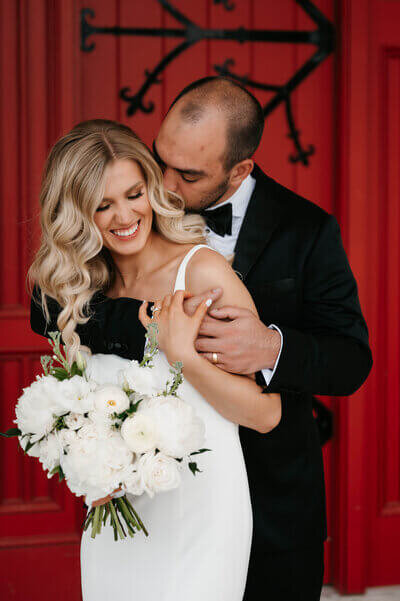 Groom kissing bride in front of red background planned by luxury wedding planner chicago